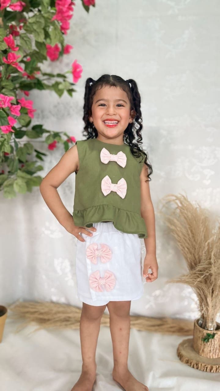 Niña con un conjunto Aurora de blusa verde oliva y short blanco